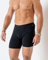 Man wearing  Black Boxer Briefs standing in a white studio room from neck to knees.