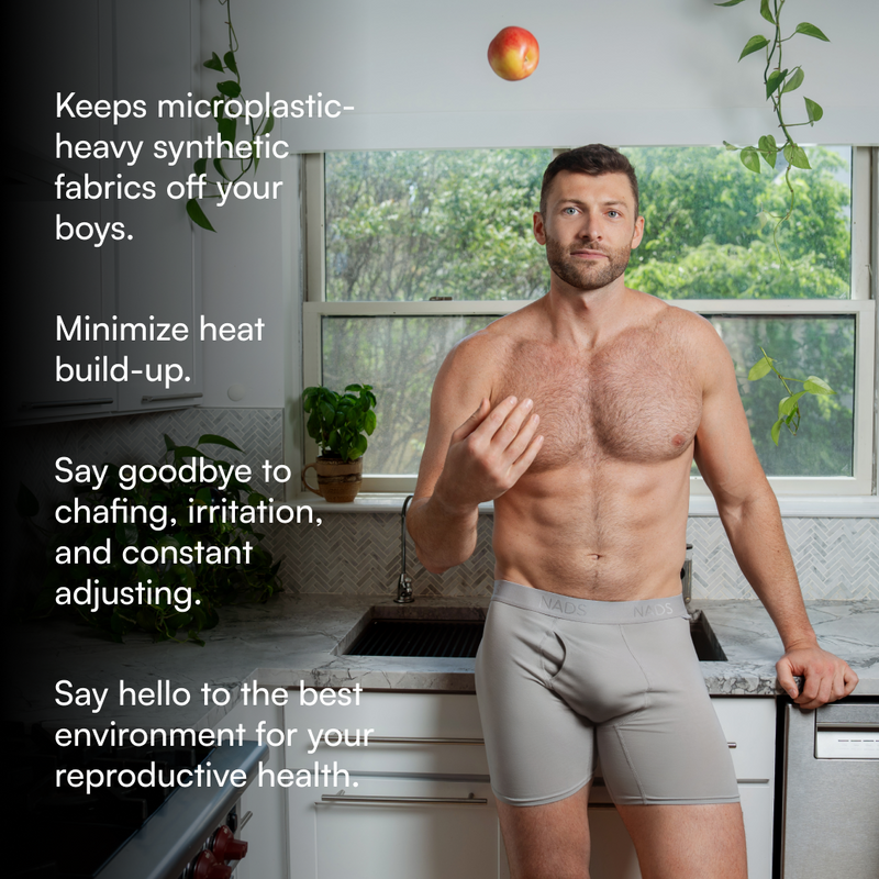 Man standing in a kitchen wearing gray boxer briefs with text about fabric benefits.