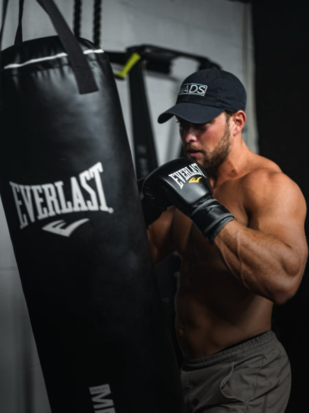 Image of young male wearing a NADS cap and boxing gloves, punching a punching bag